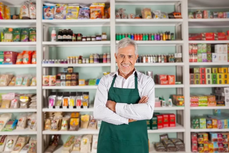 man in apron standing in front of grocery store shelves