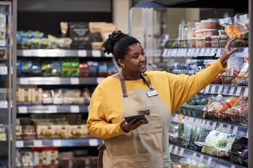 woman reaching onto shelf while checking inventory on ipad